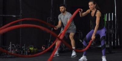 Athletic young couple with battle rope doing exercise in functional training fitness gym